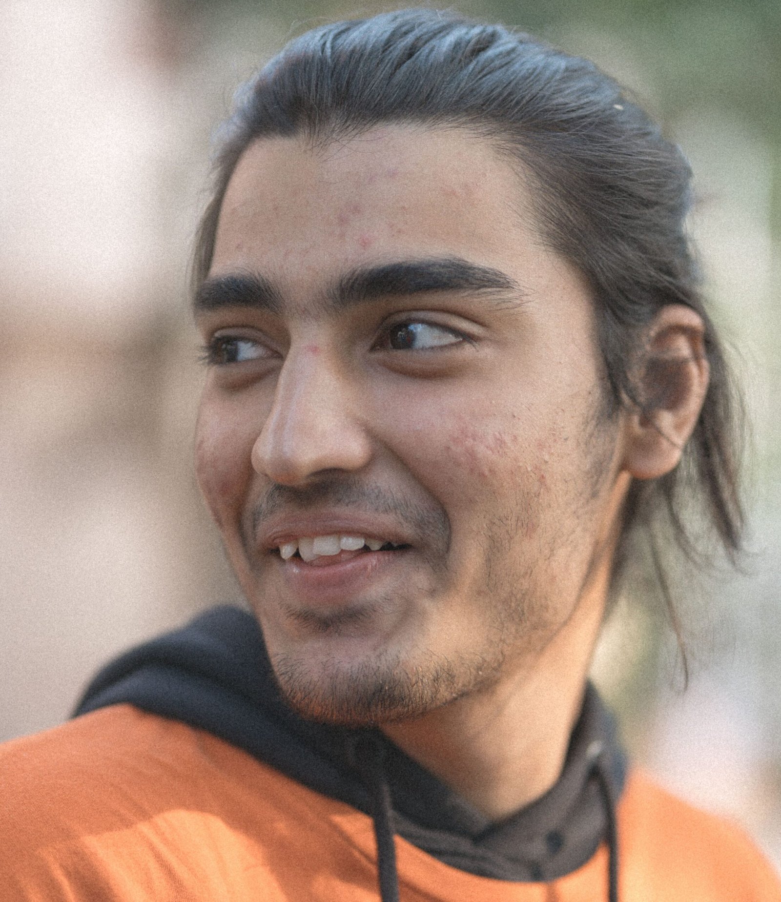 Home Close-up of a young man in an orange hoodie smiling, showcasing a natural candid expression.